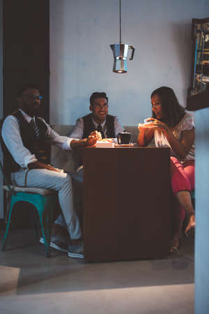 Adult woman drinking coffee at table with two men with vintage coffee maker hanging aboveの写真素材