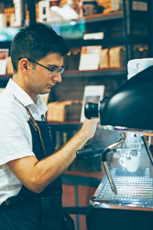 Side view of bartender in glasses and apron making espresso at coffee machineの写真素材