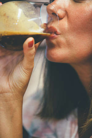 Close-up of adult woman drinking fresh black coffee from wine glass