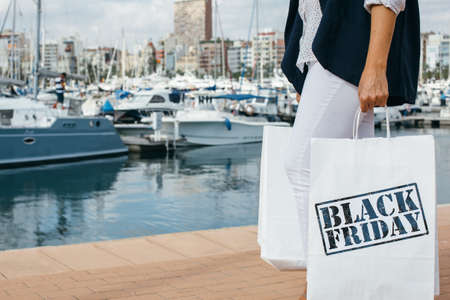 Unrecognizable female carrying two white bags with Black Friday words on them in harbor. Copyspaceの写真素材