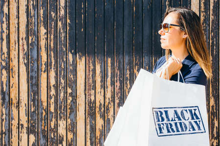 Side view of woman holding shopping bags over wooden background on Black Friday. Copyspace