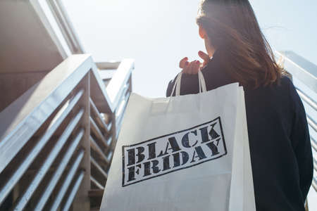 Rear view of incognito brunette holding Black Friday shopping bag while standing outdoors. Copyspaceの写真素材