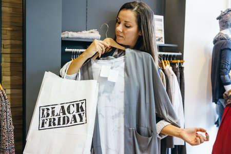 Woman with Black Friday paper bag trying new blouse while shopping. Copyspaceの写真素材
