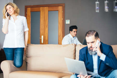 Woman and man talking on cell while young colleague working on laptop