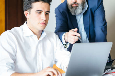 Unrecognizable bearded boss showing young manager something on laptop