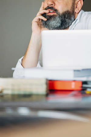 Close-up of bearded businessman at table with laptop and books