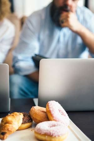 Close-up of donuts and other treats on plate on table against of unfocused businesspeople and...