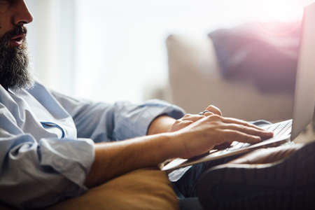 Side view of unrecognizable bearded man typing on laptop.Backlit.の写真素材