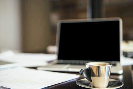 Close-up of silver cup of coffee on table against of laptopの写真素材