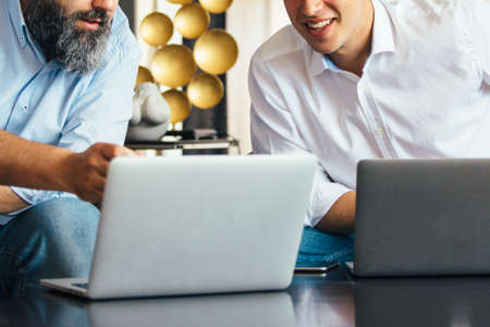 Close-up of young and adult co-workers using laptops at table