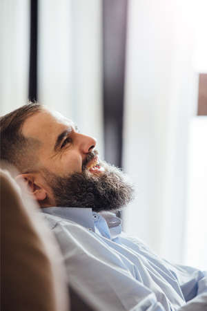 Side view of bearded businessman laughing while sitting on sofaの写真素材