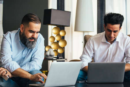 Bearded man and young colleague working on laptopsの写真素材