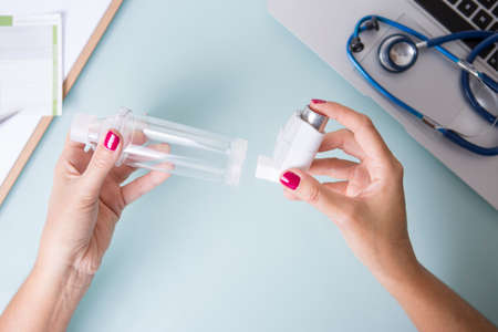 Top view of a close up of the hands of a female doctor is inserting a pressurized cartridge inhaler...