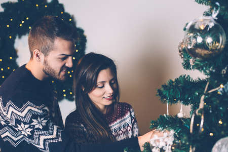Loving couple in sweaters decorating fir tree in living room.の写真素材