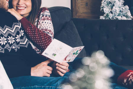 Merry couple in sweaters sitting together and reading Christmas greeting-card. の写真素材