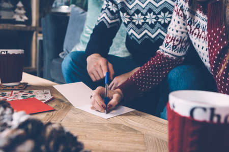 Young couple in sweaters enjoying Christmas atmosphere while writing greetings. の写真素材