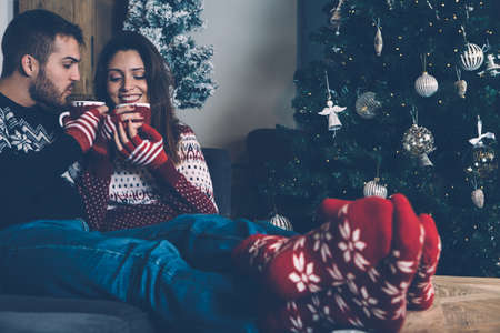 Young couple in sweaters enjoying hot drink and Christmas atmosphere at home. の写真素材