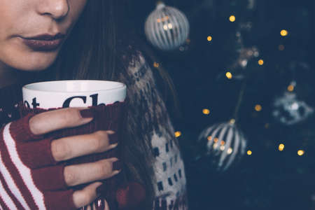 Crop shot of young girl enjoying hot drink against decorated Christmas-tree. 