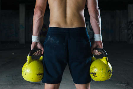 Sportsman holding two big yellow dumbbells. Horizontal indoors shotの写真素材