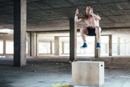 Front view of man with naked torso doing box jumps. Horizontal indoor shotの写真素材