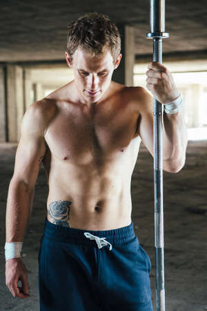 Front view of strong man standing with crossbar in hand in abandoned building.の写真素材