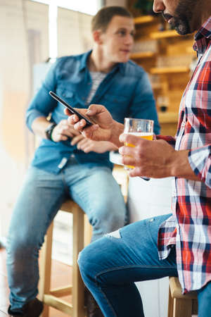 Close-up of unrecognizable bearded man chatting over phone while his friend sitting with beerの写真素材