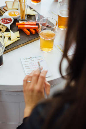 Unrecognizable woman holding pen while list of beer rating on table with snacksの写真素材