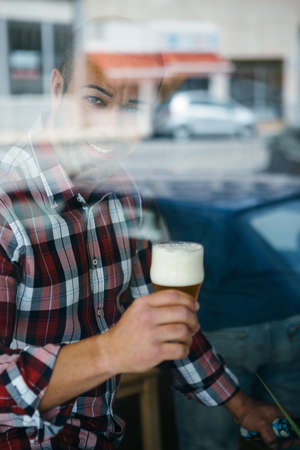 Portrait of smiling bearded man with froth beer looking at camera from behind the window