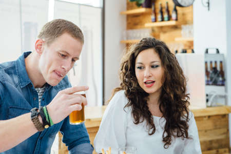 Blond man drinking craft beer with froth on mouth.Brunette looking at glassの写真素材