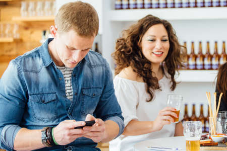 Handsome man typing on cell while sitting at table near smiling brunette