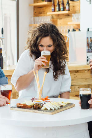 Portrait of brunette tasting craft beer at table with snacksの写真素材