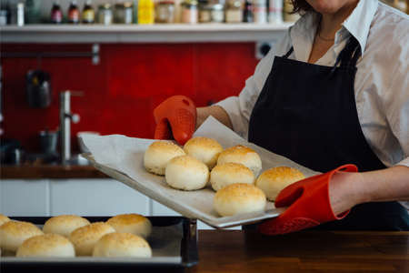 Unrecognizable baker with baked buns with sesame on tray