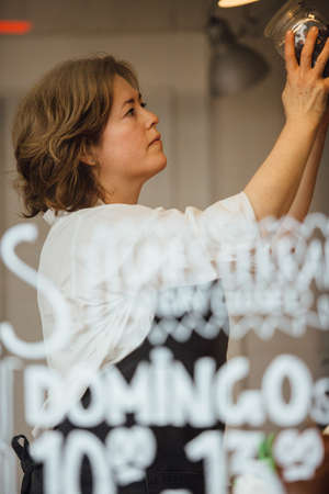 Side view of adult worker putting jar on shelf.From behind the windowの写真素材