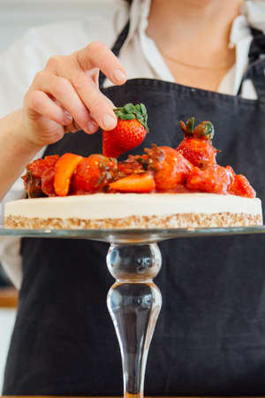 Unrecognizable confectioner decorating cake with strawberry on cakestand