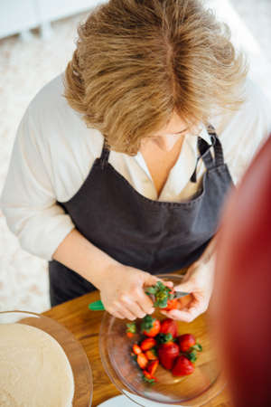 Female cook preparing strawberry for cake jam. From aboveの写真素材
