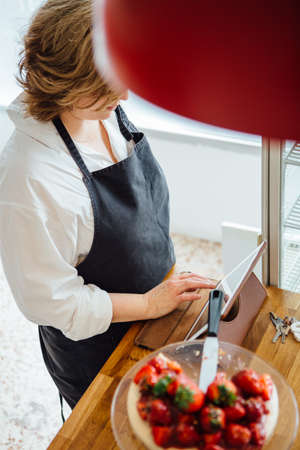 View on female confectioner using pad at counter with strawberry cakeの写真素材