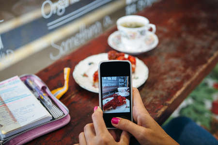 Close up of unrecognizable woman taking photo with a mobile phone of strawberry cake in cafeの写真素材