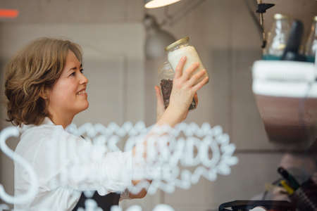 Side view of adult worker smiling while putting jars with cereals on shelfの写真素材