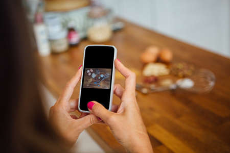 Unrecognizable woman with phone taking photo of uncooked ingredients on table.Unfocused backgroundの写真素材