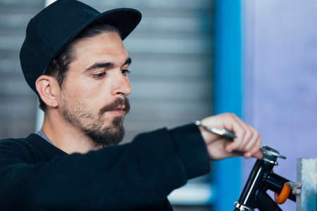 Bearded young man in black cap constructing bikeの写真素材