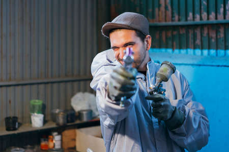 Close-up of smiling bearded craftsman holding paint gun while looking at cameraの写真素材