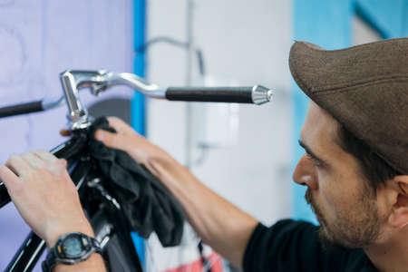 Side view of bearded craftsman in cap cleaning bike with towelの写真素材