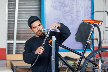 Young bearded man in black cap working with bicycleの写真素材