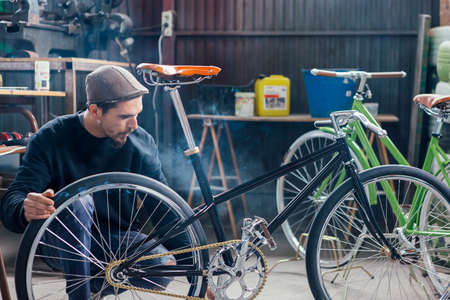 Bearded man looking at his new bicycle while smoking at workplace