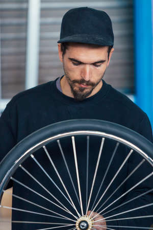 Close-up of serious bearded craftsman looking at bicycle wheelの写真素材