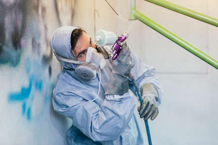 Adult man with painted gun in process of painting bikes frame in green color
