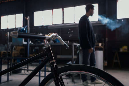 Close-up of new constructed bicycle and smoking craftsman on backgroundの写真素材