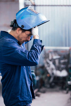 Bearded craftsman looking down while holding protective mask on head.Bokehの写真素材