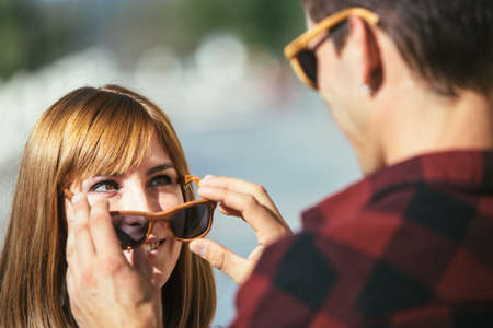 Young woman smiling to man taking off her sunglasses and looking at each other. の写真素材