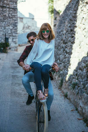Young romantic couple in sunglasses riding bicycle together at street and laughing.